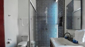 Une salle de bain avec douche, toilettes, lavabo et carrelage à motifs.