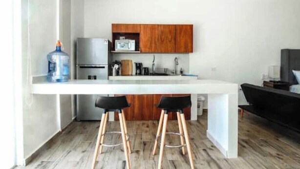 Une cuisine moderne avec un plan de travail blanc, des armoires en bois et un réfrigérateur en acier inoxydable. On trouve deux tabourets de bar noirs devant le plan de travail.