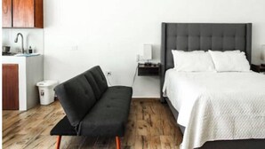 Une chambre d’hôtel moderne équipée d’un lit, de tables de chevet, d’un canapé, d’un petit coin cuisine et d’une poubelle.
