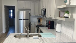 Una cocina moderna con gabinetes blancos, un refrigerador de acero inoxidable, una isla integrada con taburetes e iluminación colgante.