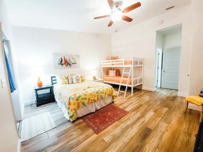 Ein Schlafzimmer mit Etagenbett, Schreibtisch, Stuhl, Deckenventilator und einem Bild an der Wand.