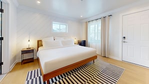 Une chambre moderne avec un grand lit, une table de chevet, un bureau et une fenêtre avec des rideaux.