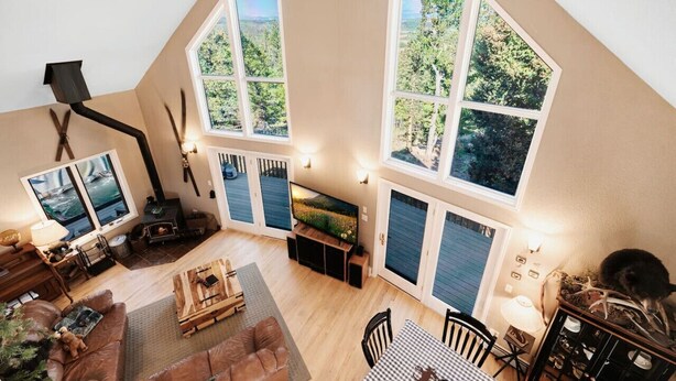 Een ruime loft met hoge plafonds, grote ramen met uitzicht op het bos, een open haard en een gezellige zithoek.