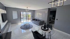 A modern living room with a grey sofa, a round dining table, and a black chair. - Knightsbridge Luxury Apartments Century City by Vvip Bookings  (Cape Town)