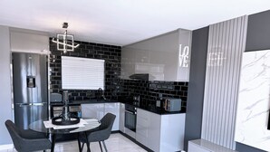 A modern kitchen with a black and white color scheme, a built-in oven, and a dining area with a round table and chairs. - Knightsbridge Luxury Apartments Century City by Vvip Bookings  (Cape Town)