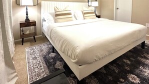 Un dormitorio ordenado con una cama, dos mesitas de noche con lámparas, un ventilador de techo y una puerta.
