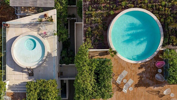 An aerial view of a resort with a large circular pool surrounded by lush greenery and a wooden deck with lounge chairs. - Ocean view Apartment PXM (Puerto Escondido)