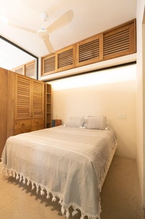 Camera da letto con un letto, un armadio in legno, una ventola a soffitto e scaffali a muro.