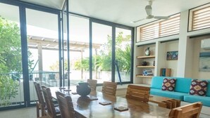 A dining area with a wooden table and chairs, a hanging light fixture, and a view of the outdoors through large windows. - Ocean view Apartment PXM (Puerto Escondido)