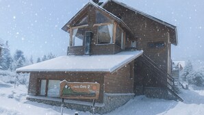 A wooden cabin with a snow-covered roof and a sign in front. - Cerro Catedral excellent studio apartment (Cerro catedral,Río Negro Province)