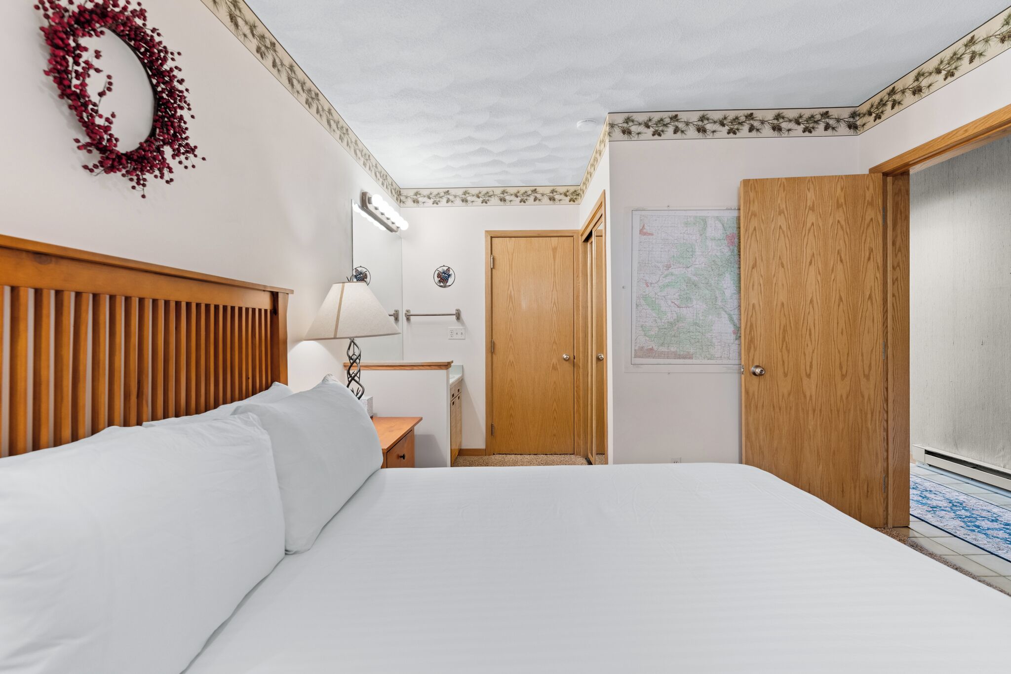 Une chambre à coucher avec un lit, une tête de lit en bois, une table de chevet, une lampe, une armoire en bois et une carte accrochée au mur.