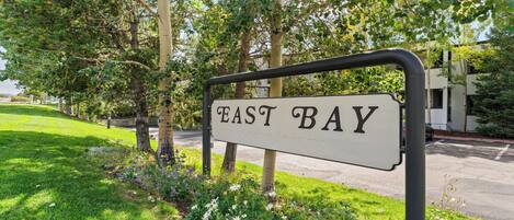 A sign reading "EAST BAY" with a metal frame, surrounded by greenery and trees.