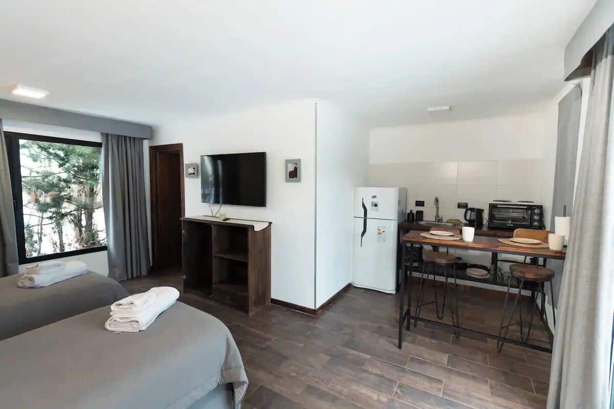 Ein modernes Hotelzimmer mit Bett, Schreibtisch, Fernseher, Kühlschrank und einer Küchenzeile.