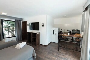 Una habitación de hotel moderna con cama, escritorio, televisor, refrigerador y kitchenette.
