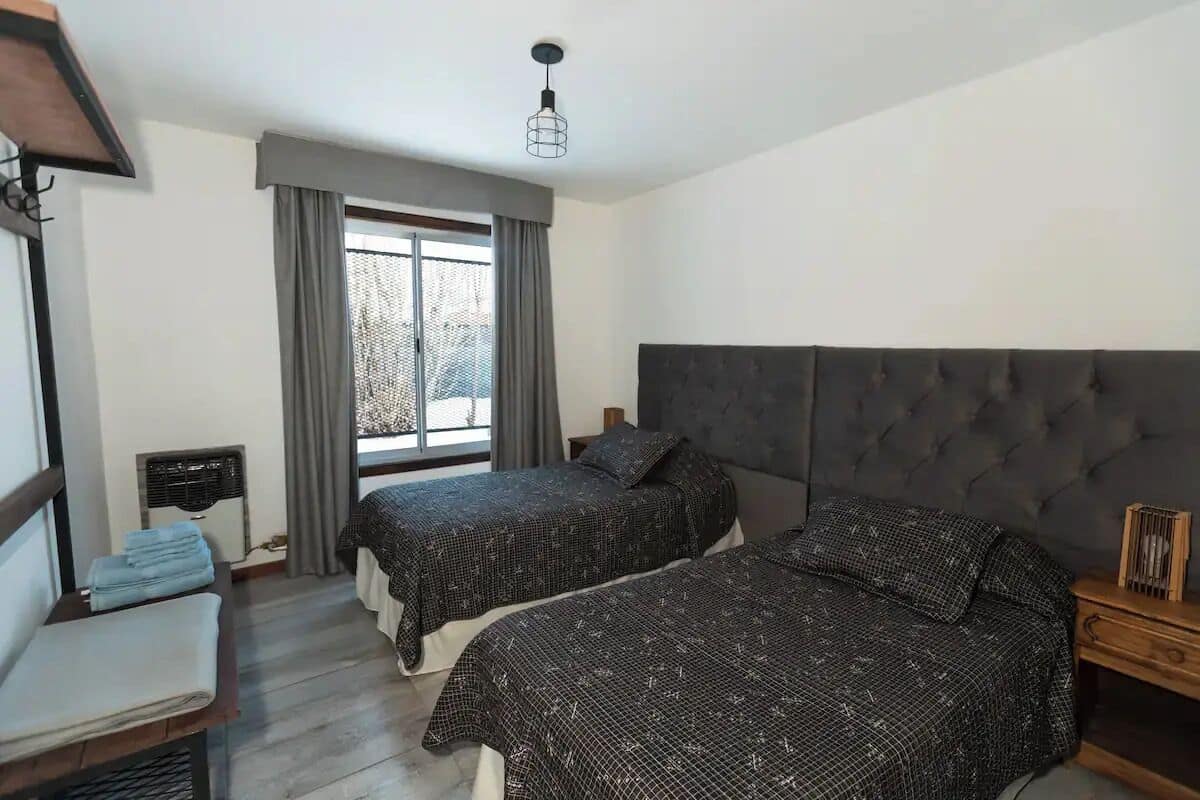Ein Schlafzimmer mit zwei Betten, einem Fenster mit Vorhängen, einem Nachttisch und einer Pendelleuchte.