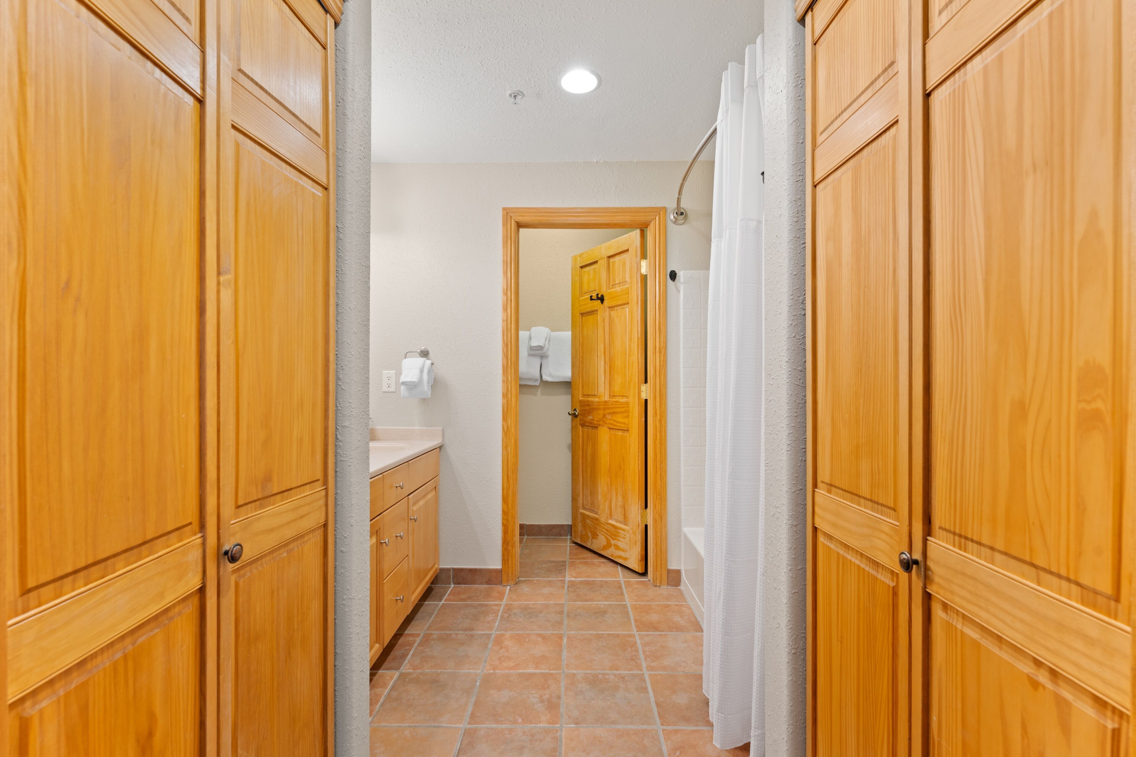 A hallway with wooden doors, a bathroom with a shower curtain, and a tiled floor.