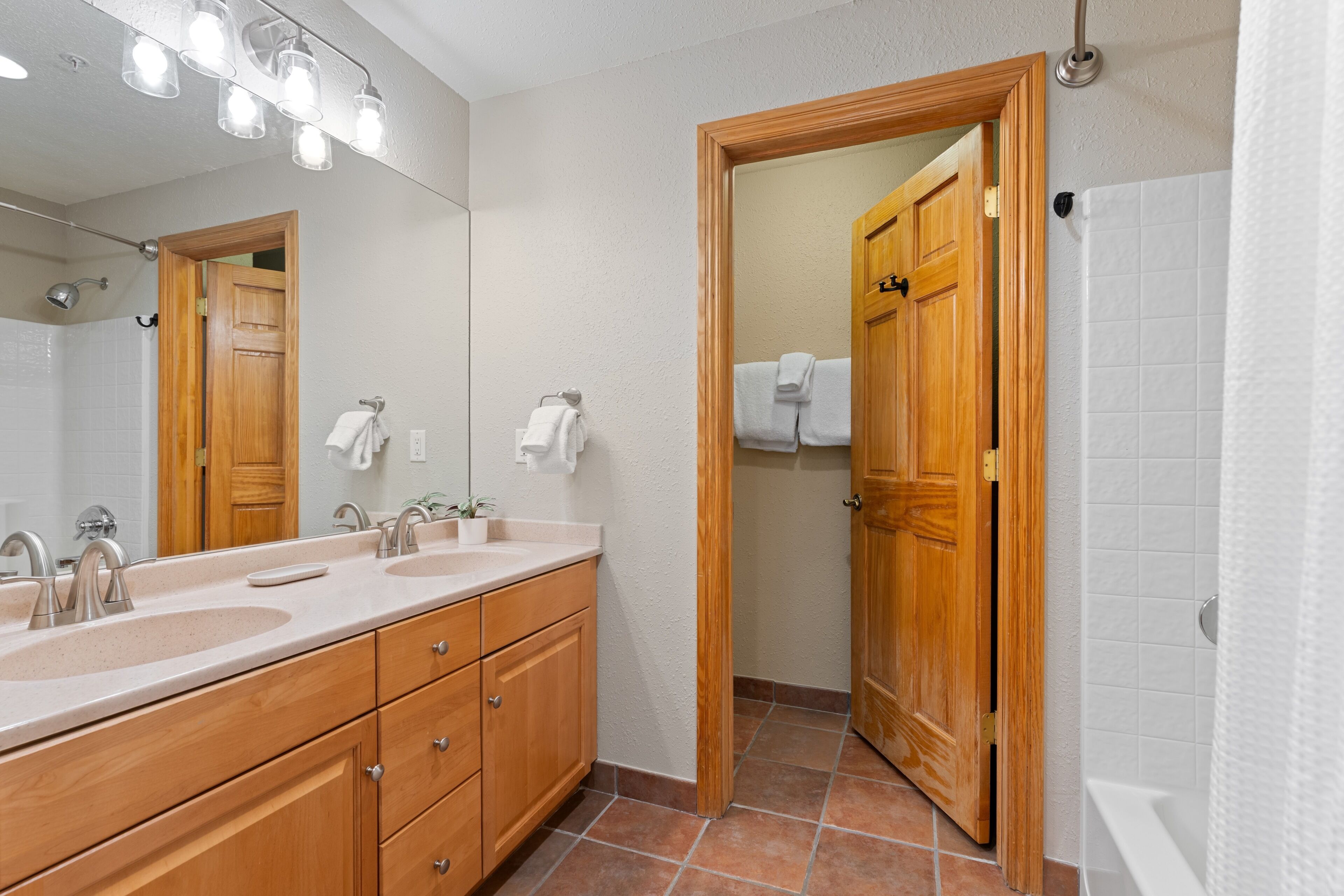 A bathroom with a wooden vanity, two sinks, a mirror, and a shower area.