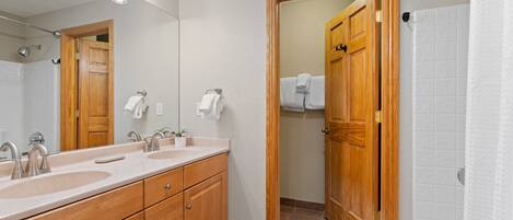 A bathroom with a wooden vanity, two sinks, a mirror, and a shower area.