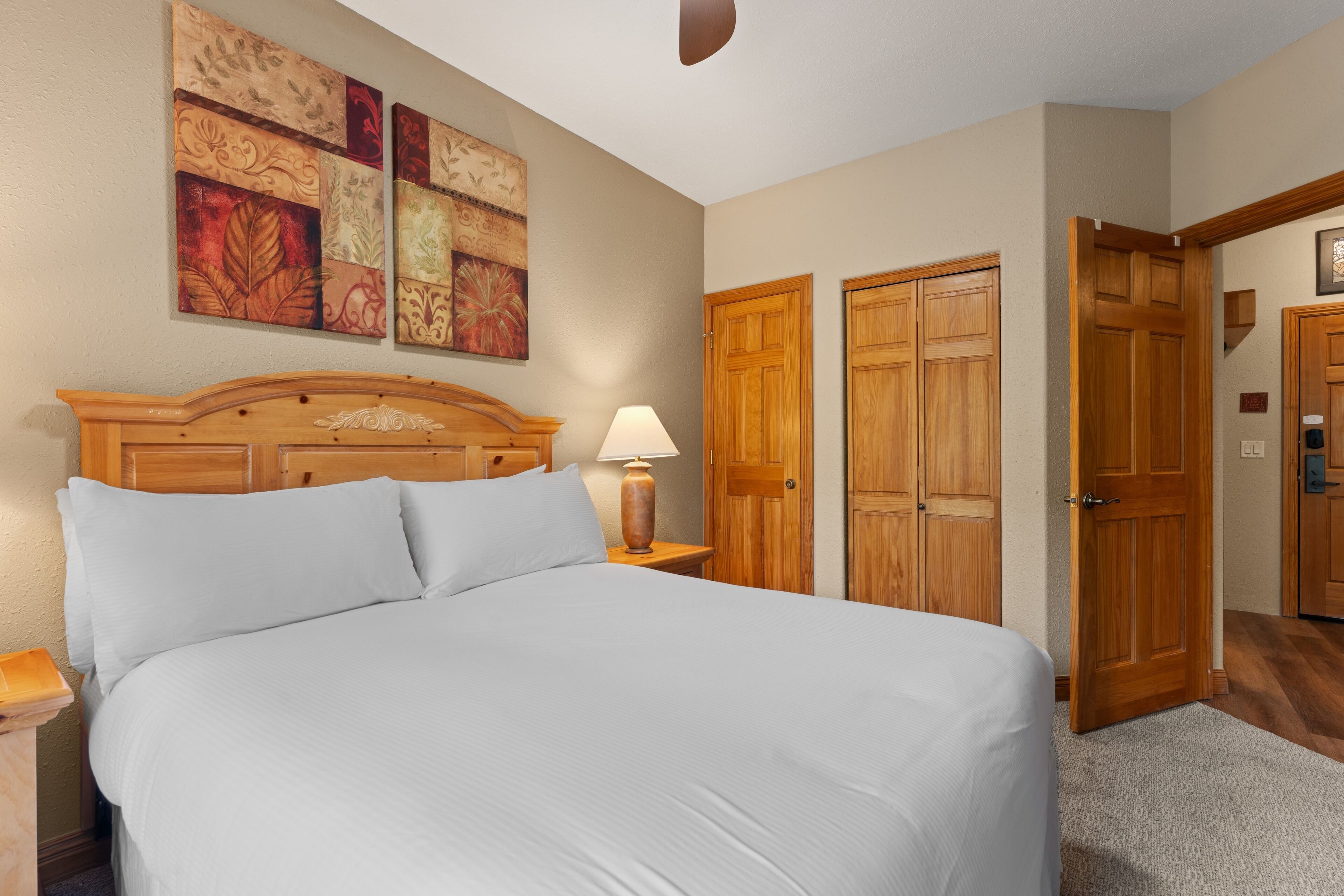 A bedroom with a large bed, wooden wardrobe, and a nightstand with a lamp.