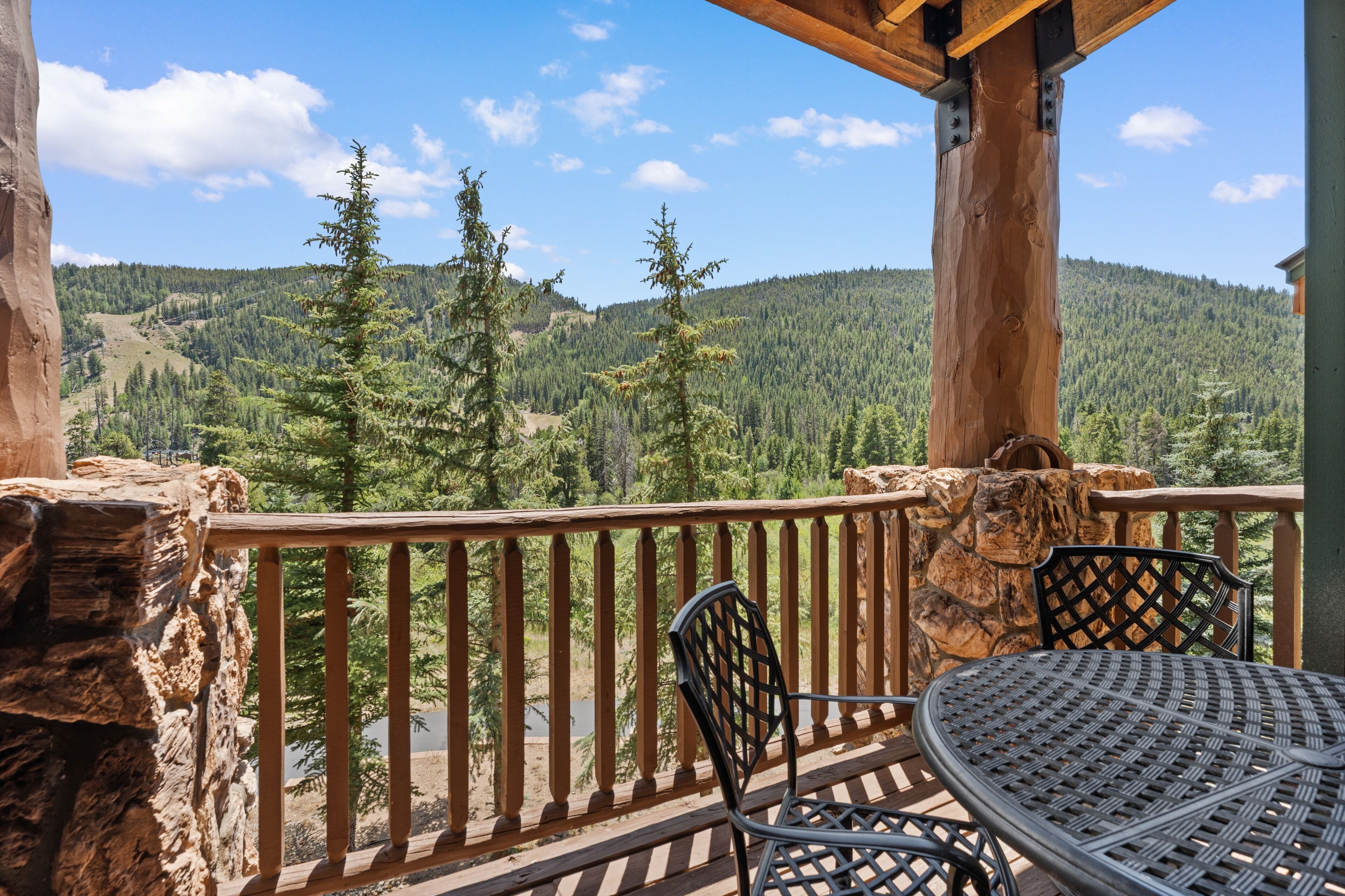 A wooden deck with a table and chairs, overlooking a forested valley.