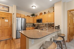 A kitchen with wooden cabinets, stainless steel appliances, a granite countertop, and a built-in island with stools. - Hr5961-2 (Keystone)