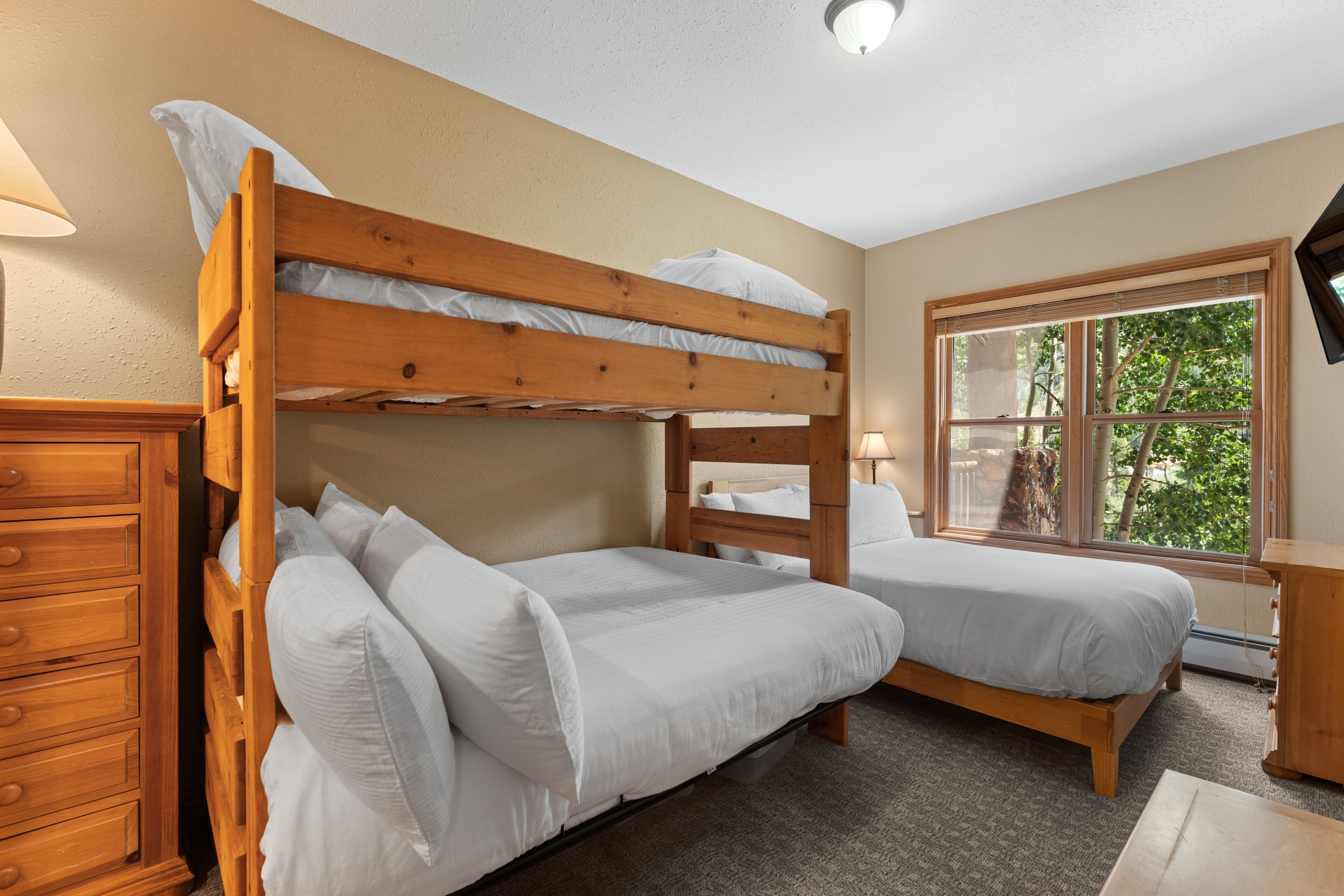A bunk bed room with a wooden dresser and a window with a view of trees.