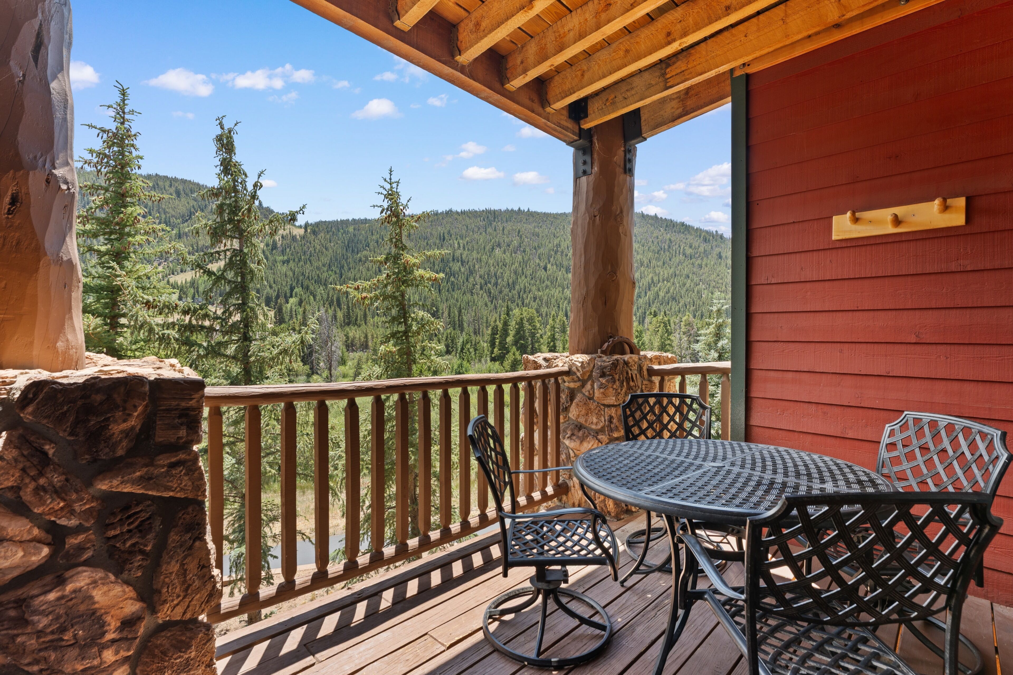 Une terrasse en bois avec une table et des chaises, offrant une vue sur une montagne boisée.