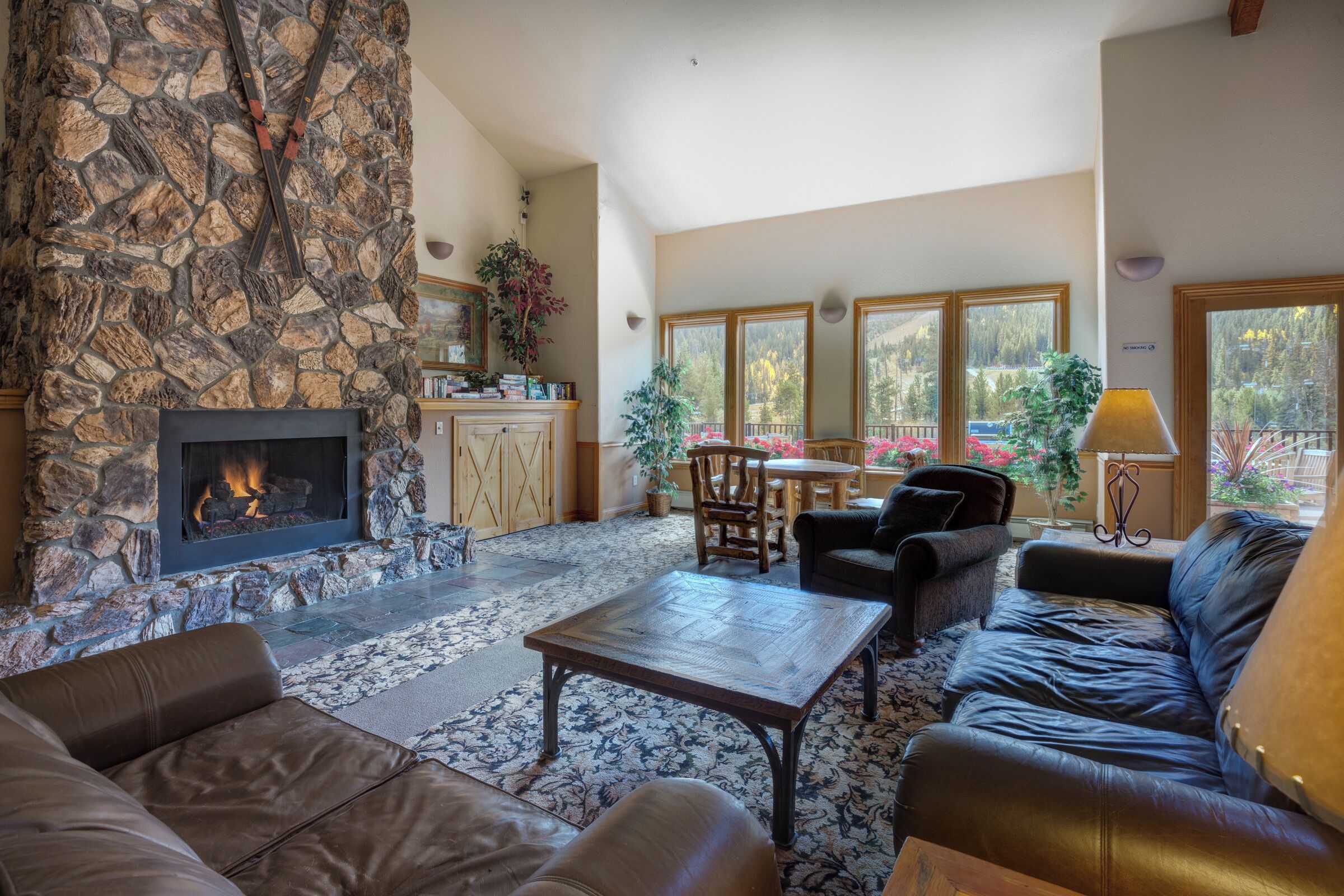 A spacious living area with a stone fireplace, leather sofas, a coffee table, and large windows offering a view of the outdoors.