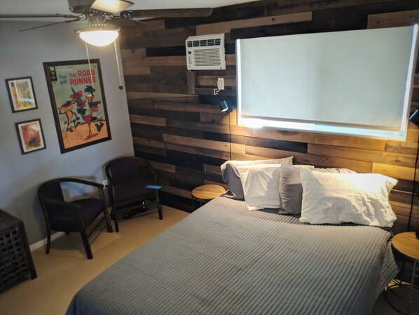 Une chambre à coucher comprenant un lit, une chaise, une petite table et un climatiseur fixé au mur.