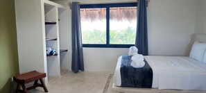 Un dormitorio con cama, armario, pequeño banco y ventana con cortinas.