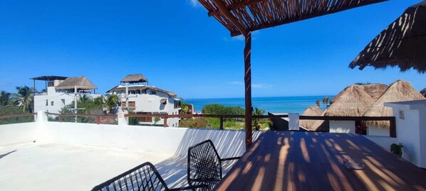 Une terrasse avec vue sur la mer, une construction à toit de chaume et un bâtiment blanc.