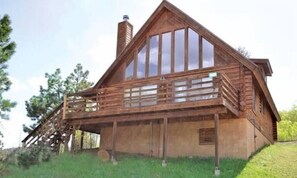 A wooden cabin with a balcony, large windows, and a chimney.