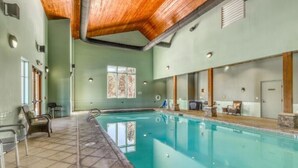 A swimming pool with a tiled floor, wooden ceiling beams, and a window with a decorative pattern. - Angel Fire | Ski Weekend Stay | Hot Tub & Mountain (Angel Fire)