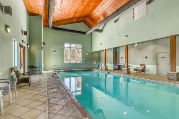 A swimming pool with a tiled floor, wooden ceiling beams, and a window with a decorative pattern.