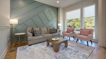 Uma sala de estar moderna com um sofá seccional, duas poltronas, uma mesa de centro e um tapete estampado.