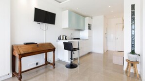 A modern kitchen with white cabinets, a black TV mounted on the wall, a wooden dining table, and a black bar stool. - Superb studio with sea and Esterel views, 2-minute walk to the beach (Cannes)