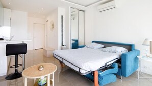 A modern bedroom with a bed, a small round table, a chair, and a wardrobe. - Superb studio with sea and Esterel views, 2-minute walk to the beach (Cannes)