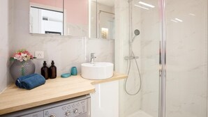 A modern bathroom with a marble shower enclosure, a sink with a mirror above, and a wooden vanity with toiletries. - Superb studio with sea and Esterel views, 2-minute walk to the beach (Cannes)