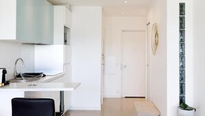 A modern kitchen with white cabinetry, a stainless steel sink, and a black chair. - Superb studio with sea and Esterel views, 2-minute walk to the beach (Cannes)