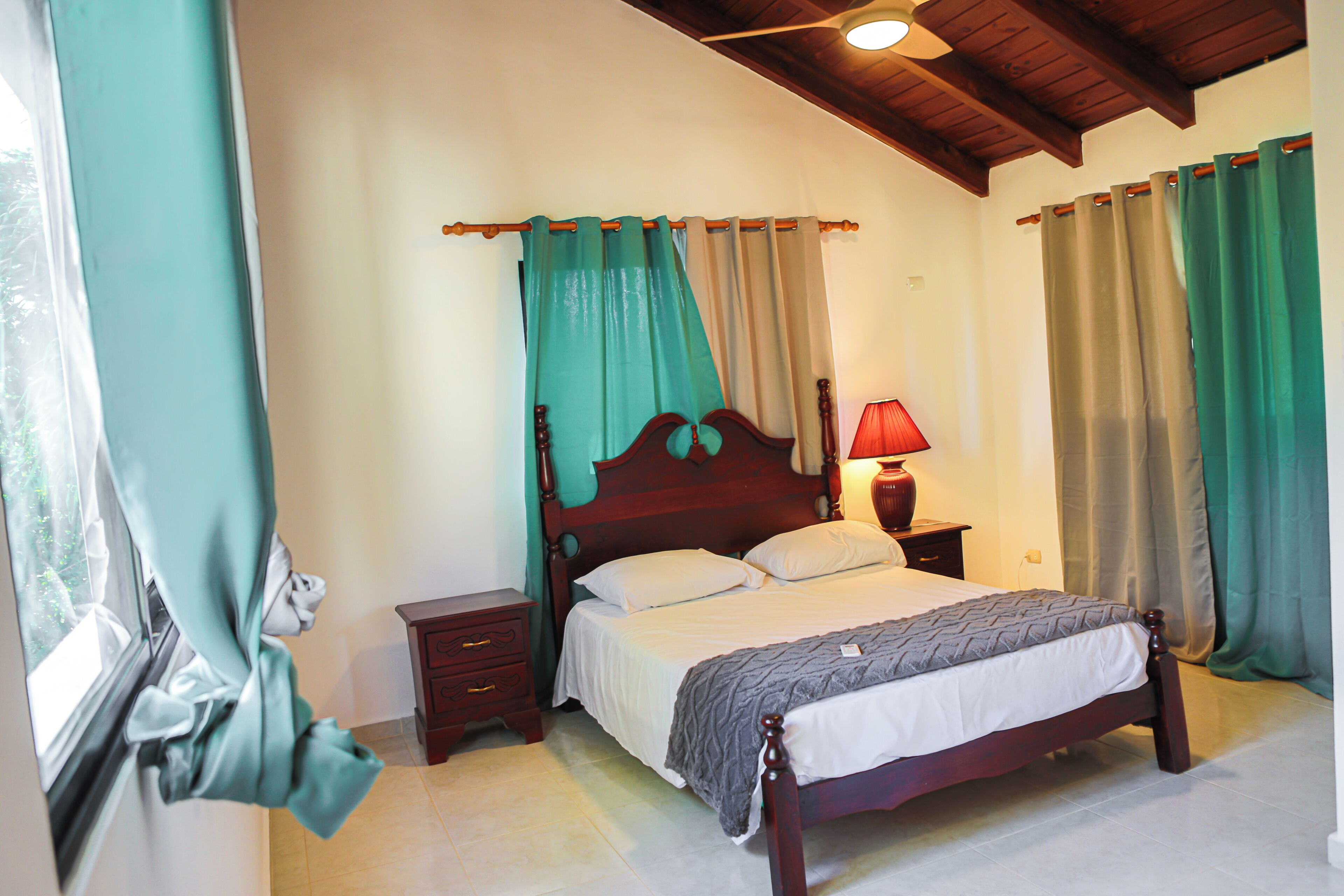 A bedroom with a wooden bed, a nightstand, a lamp, and curtains.