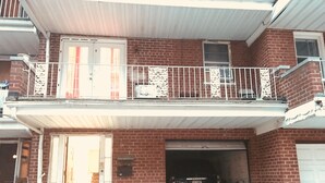 Un bâtiment de deux étages en briques, avec une porte de garage ouverte, une voiture garée et un balcon doté d’une balustrade.