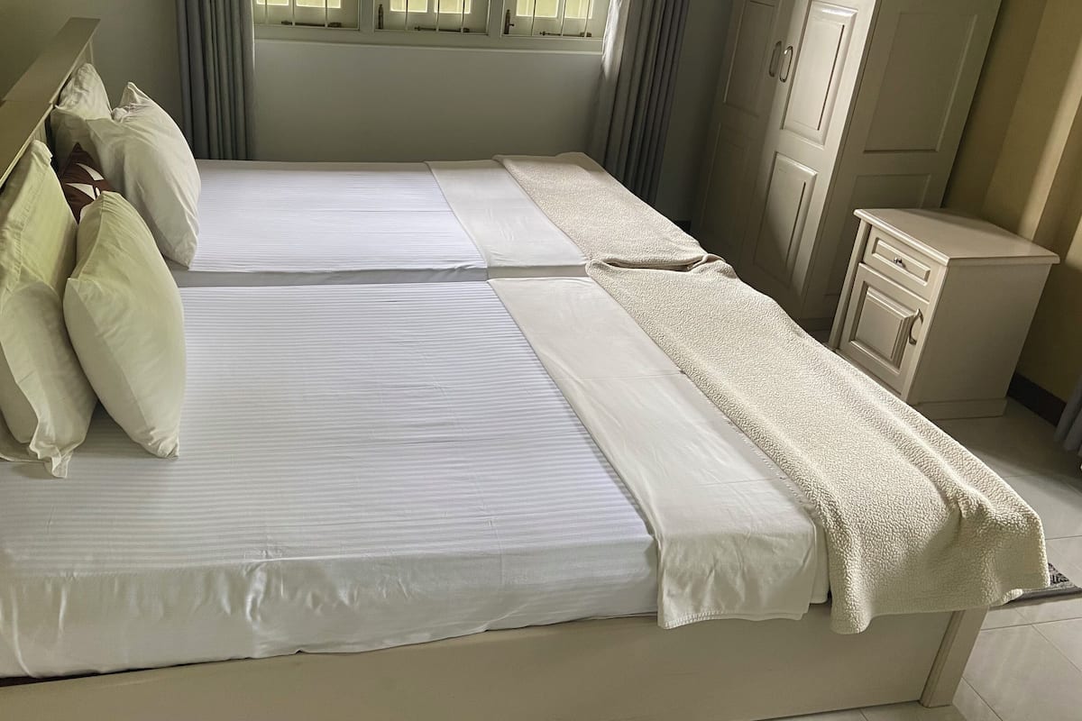 A double bed with white linens and pillows, a bedside table, and a wardrobe in a hotel room.