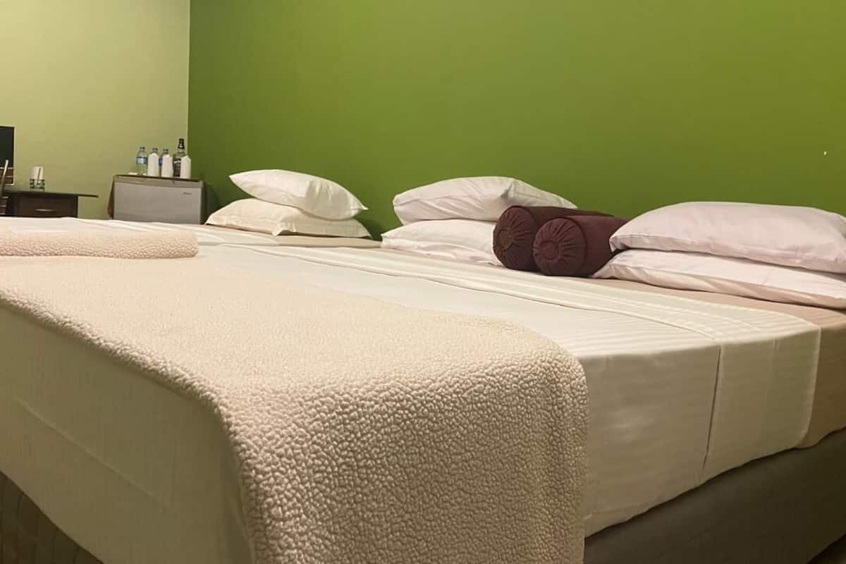A neatly made bed with white and brown pillows, a beige blanket, and a green wall in the background.