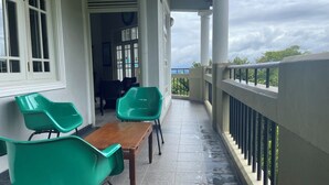 A balcony with a wooden table and two green chairs, a white railing, and a view of the sea. - VISTA HOUSE (Kandy)