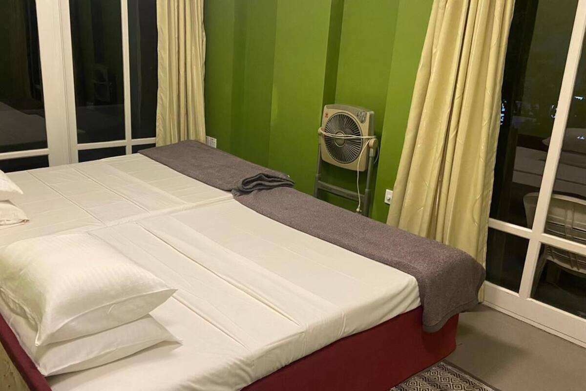 A room with a bed, pillows, a fan, and curtains.