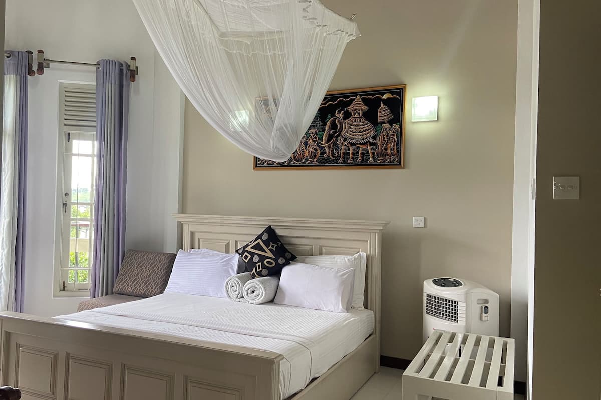 A bedroom with a bed, a window with curtains, a wall-mounted air conditioner, and a decorative painting.