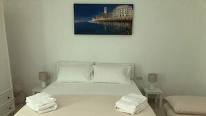 A bedroom with a large bed, two bedside tables with lamps, a painting of a coastal scene, and a view of the sea. - Charming 1-bedroom apartment with WiFi, AC in amazing Bari (Bari)