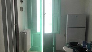 A small kitchen with a white refrigerator, a table with two chairs, and a teal door. - Charming 1-bedroom apartment with WiFi, AC in amazing Bari (Bari)