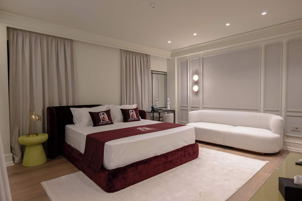 A modern bedroom with a large bed, a white sofa, and a small table with a lamp.