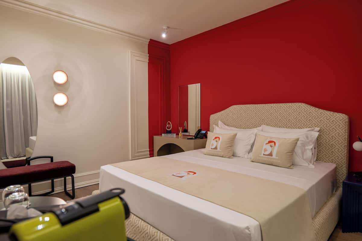A hotel room with a large bed, a desk, a chair, and a mirror.